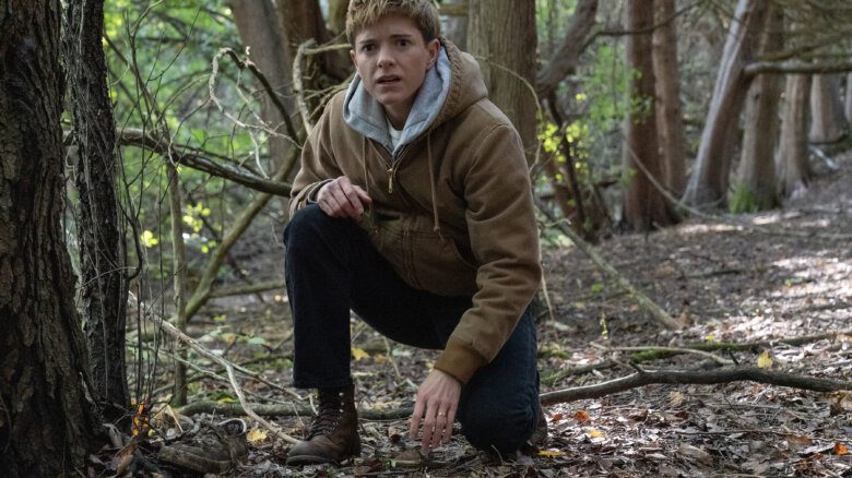 Mae Martin kneeling in a forest.