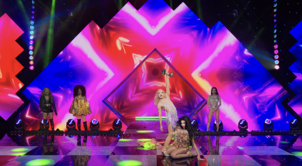 Brigiding raising an air blower and standing behind a kneeling Viñas Deluxe on the stage